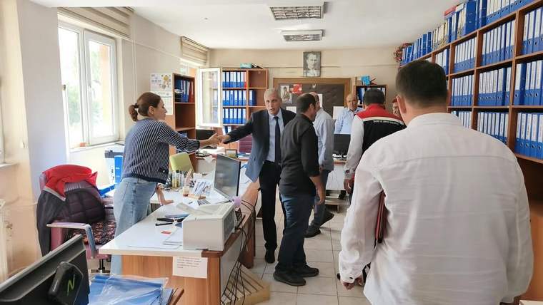 Bir ofiste, birkaç kişi arasında el sıkışma gerçekleşiyor; masada dosyalar ve bilgisayarlar var.