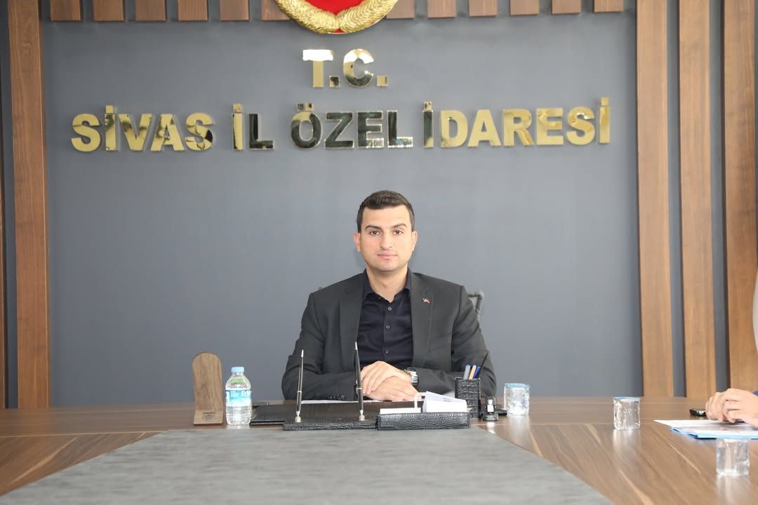 Sivas İl Özel İdaresi toplantı odasında oturan bir kişi, masanın arkasında duruyor.