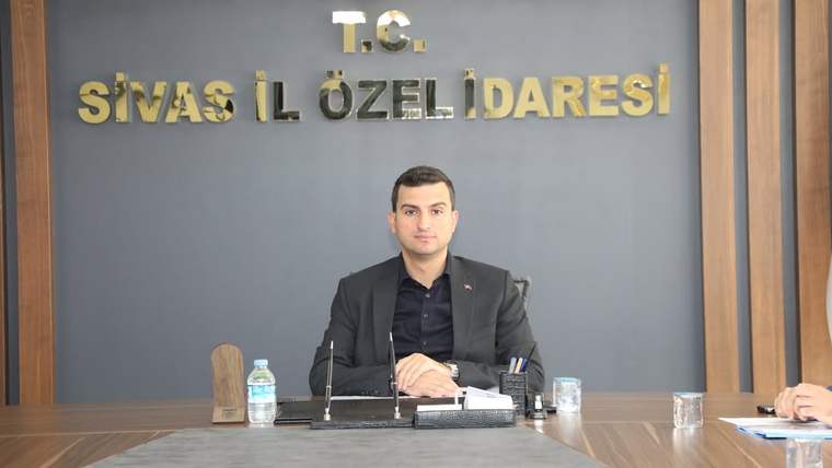 Sivas İl Özel İdaresi toplantı odasında oturan bir kişi, masanın arkasında duruyor.