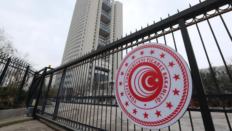 Siyah demir parmaklıkta Ticaret Bakanlığı yazılı yuvarlak logo, arkasında yüksek katlı bina görülüyor.