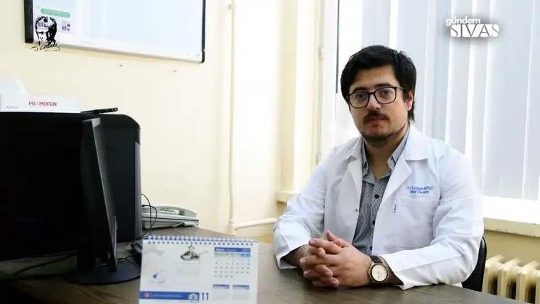 Beyaz önlük giymiş bir doktor, masa başında oturuyor ve bilgisayar ekranına bakıyor.