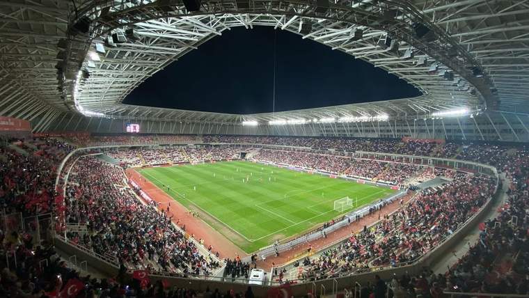 Üzeri kapalı stadyumda futbol maçı oynanırken tribünlerde çok sayıda taraftar görülüyor.