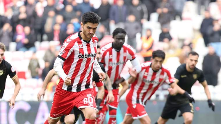 Kırmızı-beyaz çubuklu formalı bir futbolcu, sahada topa doğru koşarken arkasında diğer futbolcular görülüyor.