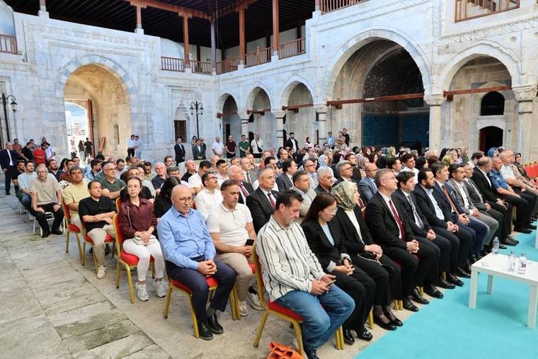 Taş kemerli tarihi avluda sıralar halinde oturan ve ayakta duran kalabalık bir grup görülüyor.