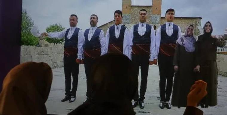 Sivas halayı çeken beş kişi, arka planda taş bir yapı ile birlikte duruyor.