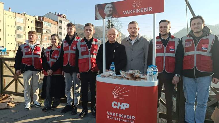 Kırmızı yelekli kişiler, üzerinde CHP Vakfıkebir İlçe Başkanlığı yazan kürsünün yanında duruyor.