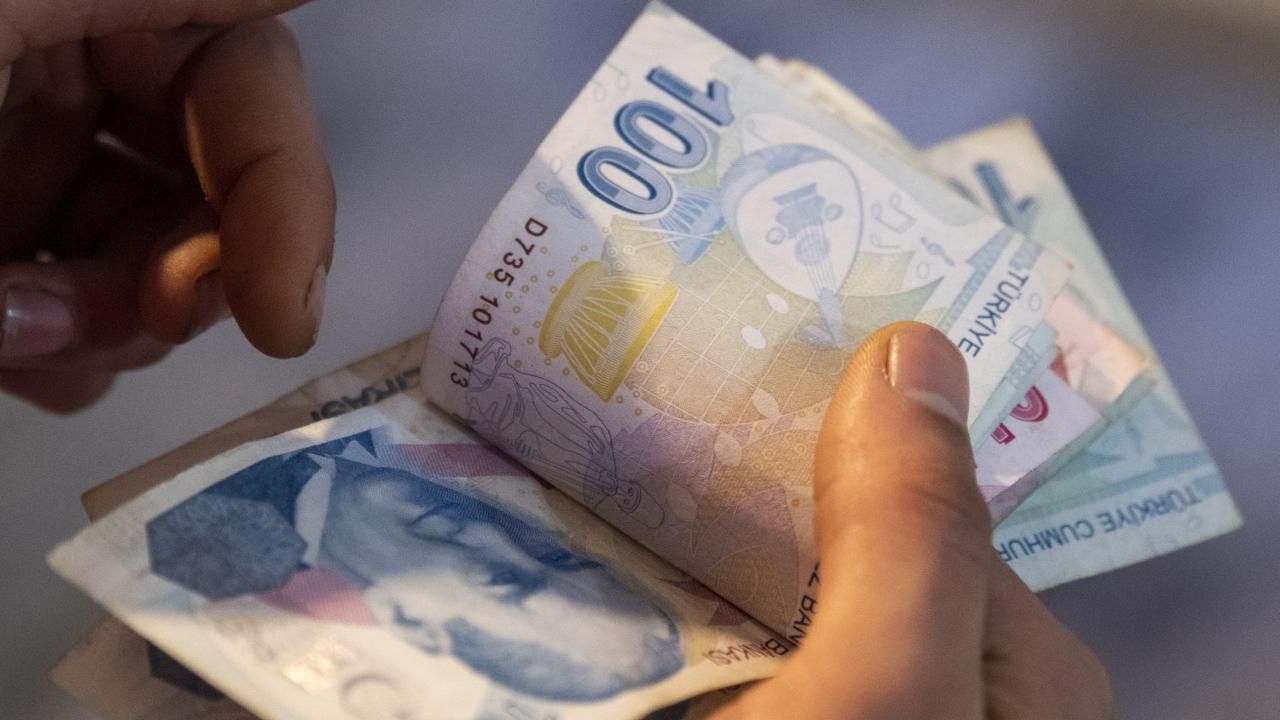 Ellerin tuttuğu farklı kupürlerde Türk lirası banknotları, yakın planda üst üste görülüyor.