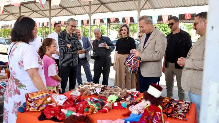 Bir grup insan, masanın üzerinde yer alan el yapımı oyuncakları inceliyor.