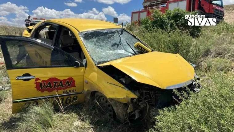 Yolda devrilmiş bir taksi aracı, etrafında yeşil bitki örtüsü var.
