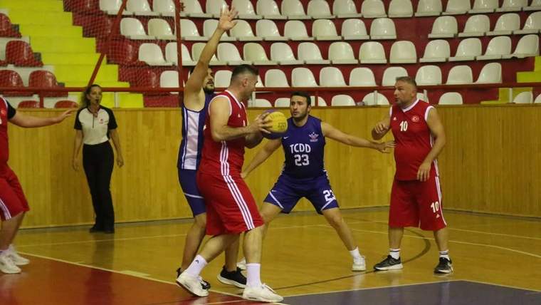 Spor salonunda kırmızı ve mor formalar giyen basketbolcular, top için mücadele ederken görülüyor.