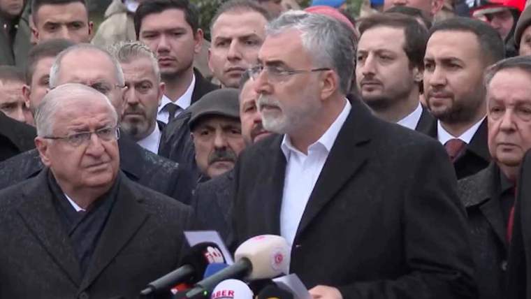 Kürsüde konuşan iki kişi, arka planda kalabalık bir grup yer alıyor.