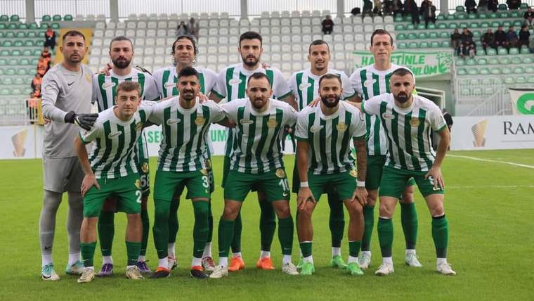 Yeşil-beyaz çubuklu formalar giyen futbolcular, stadyum sahasında takım fotoğrafı için poz veriyor.