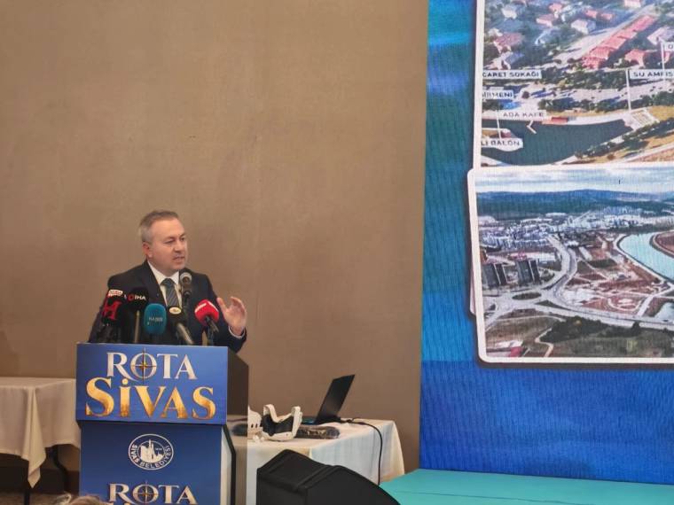 Kürsüde konuşan bir kişi, önünde “Rota Sivas” yazılı pano ve yanında gezi görüntülerinin yer aldığı ekranla görülüyor.