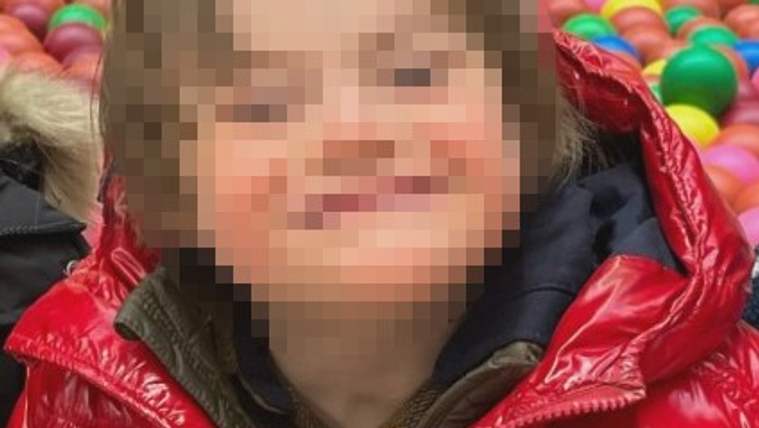 Kırmızı bir mont giymiş, gülümseyen bir çocuk, arka planda renkli toplarla dolu bir alan var.