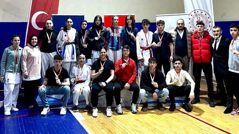 Madalyalı sporcular, antrenörler ve yöneticiler spor salonunda Türk bayrağı önünde toplu poz veriyor.