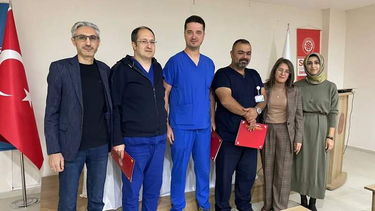 Türk bayrağı ve kırmızı kurum bayrağı önünde, aralarında sağlık çalışanlarının da bulunduğu yedi kişi poz veriyor.