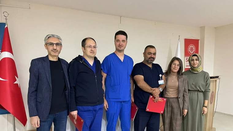 Türk bayrağı ve kırmızı kurum bayrağı önünde, aralarında sağlık çalışanlarının da bulunduğu yedi kişi poz veriyor.