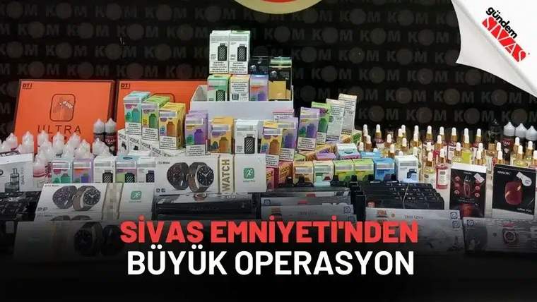 Masa üzerinde çok sayıda kutu, şişe, elektronik cihaz ve çeşitli ürünler sergileniyor; arkada KOM yazıları bulunuyor.