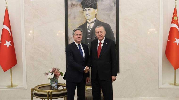Cumhurbaşkanı Erdoğan ve bir kişi, el sıkışırken bir portre arka planda görünüyor.