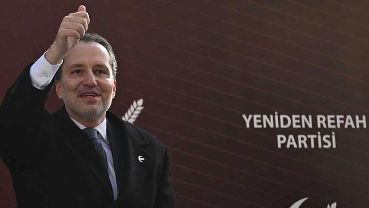 Bir kişi, sağ elini yukarı kaldırarak onay işareti yapıyor, arka planda parti logosu ve yazılar var.