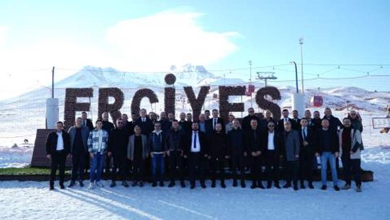 Karlı zeminde, arkasında büyük harflerle “ERCIYES” yazısı bulunan dağ önünde toplu duran kişiler