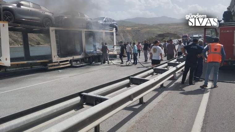 Yolda duran bir tırın üstünde yanmakta olan araçlar ve etrafında toplanmış insanlar.