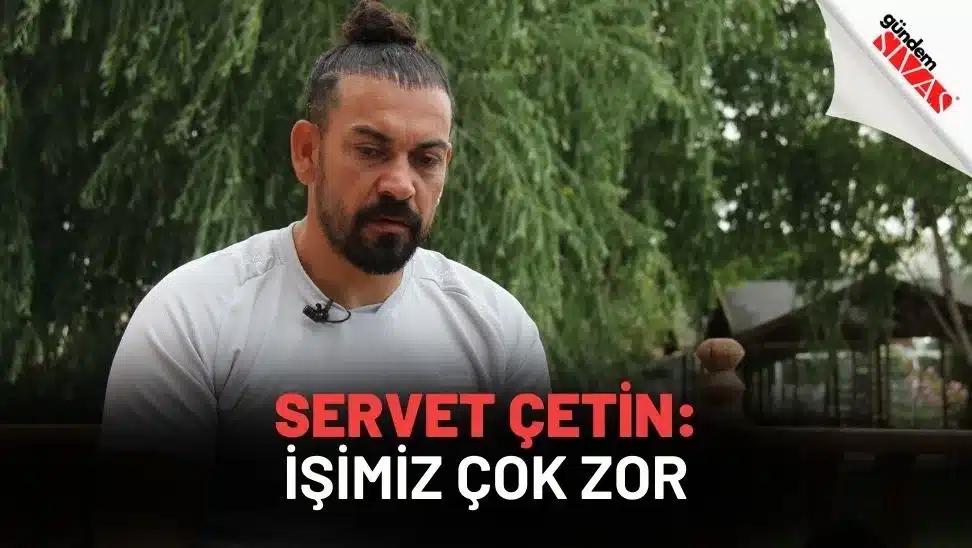 Bir kişi, açık havada otururken düşünceli bir şekilde kameraya bakıyor.