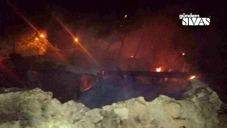 Gece karanlığında, kar yığınlarının arkasındaki yapıda alevler ve yoğun duman yükseliyor.