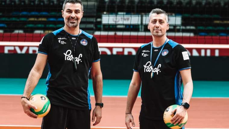 Voleybol antrenörleri, salon içinde top tutarak poz veriyor.