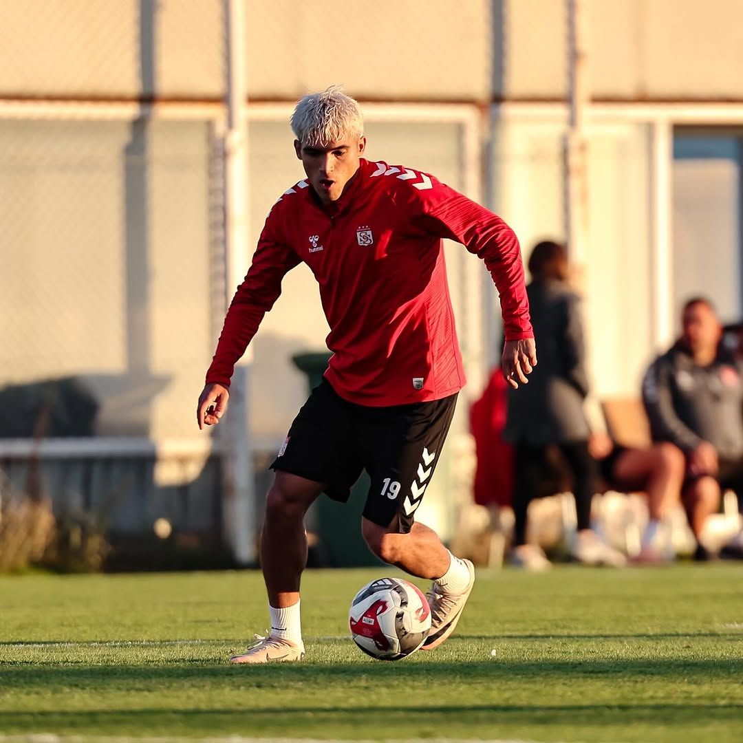 Kırmızı forma giymiş bir futbolcu, antrenman sahasında top sürüyor.