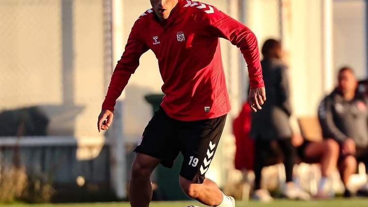 Kırmızı forma giymiş bir futbolcu, antrenman sahasında top sürüyor.