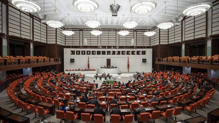 Büyük bir meclis salonunda sıralarda oturan çok sayıda kişi ve önde kürsülerin bulunduğu genel görünüm.