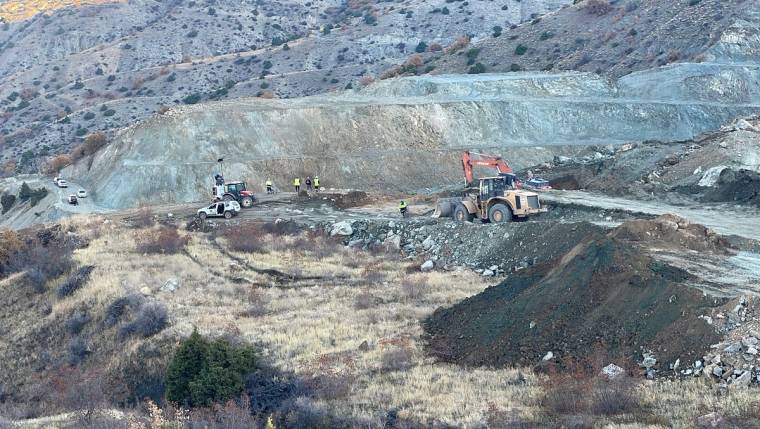 Kayalık bir yamaçta iş makineleri ve işçiler, geniş bir kazı alanında çalışırken görülüyor.
