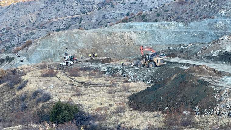 Kayalık bir yamaçta iş makineleri ve işçiler, geniş bir kazı alanında çalışırken görülüyor.