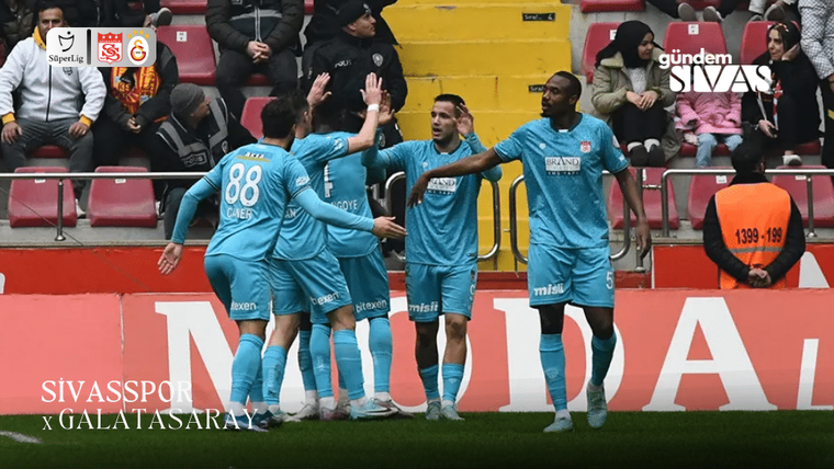 Futbol sahasında turkuaz formalı oyuncular, tribünlerin önünde el ele vererek kutlama yapıyor.