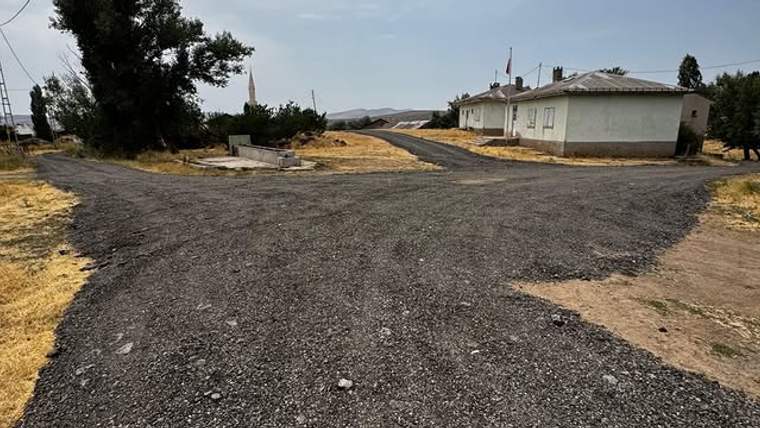 Kırsal yerleşimde yeni serilmiş stabilize yollar, tek katlı bir bina ve ağaçların arasında uzanıyor.
