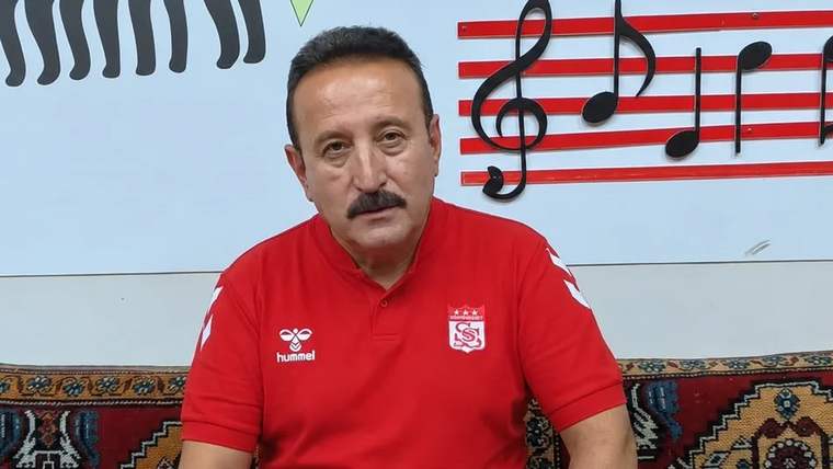 Kırmızı tişört giymiş bir kişi, arkasında müzik notaları ve desenler bulunan bir duvarın önünde oturuyor.