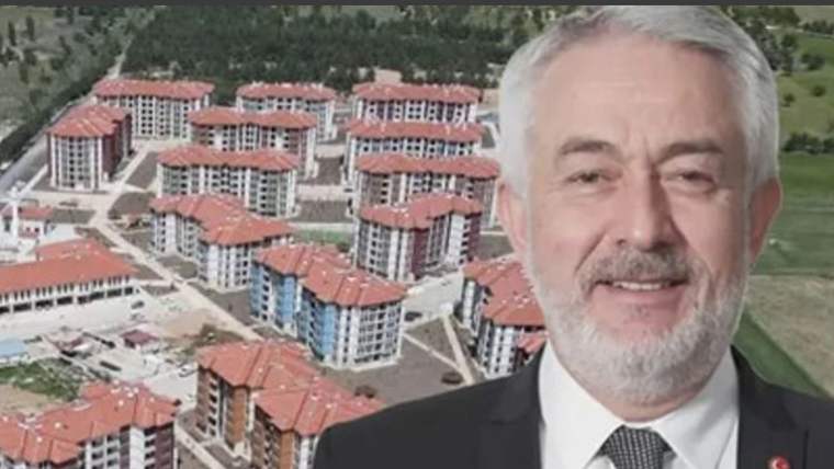 Kırmızı çatılı çok katlı konut binalarının önünde takım elbiseli, beyaz saçlı ve sakallı bir adam görülüyor.
