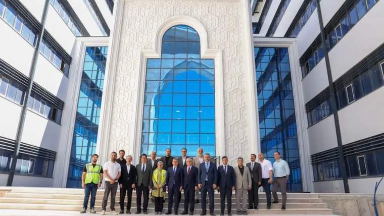 Geniş camlı modern bir binanın merdivenlerinde, aralarında iş güvenliği yeleği giyen kişinin de bulunduğu grup duruyor.