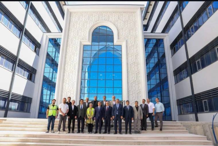 Geniş camlı modern bir binanın merdivenlerinde, aralarında iş güvenliği yeleği giyen kişinin de bulunduğu grup duruyor.