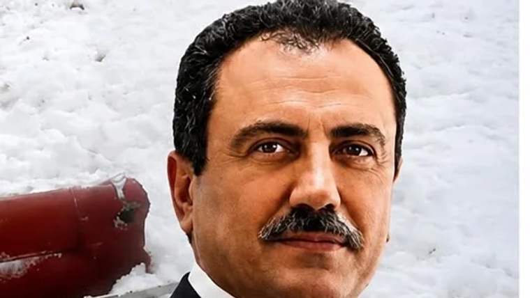 Bir adam, beyaz bir arka planda gülümseyerek poz veriyor. Adamın sakalı ve bıyığı var.