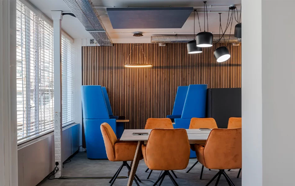 Mavi ve turuncu renklerde oturma alanları, ahşap duvar ve modern aydınlatmalarla döşenmiş bir ofis iç mekan.