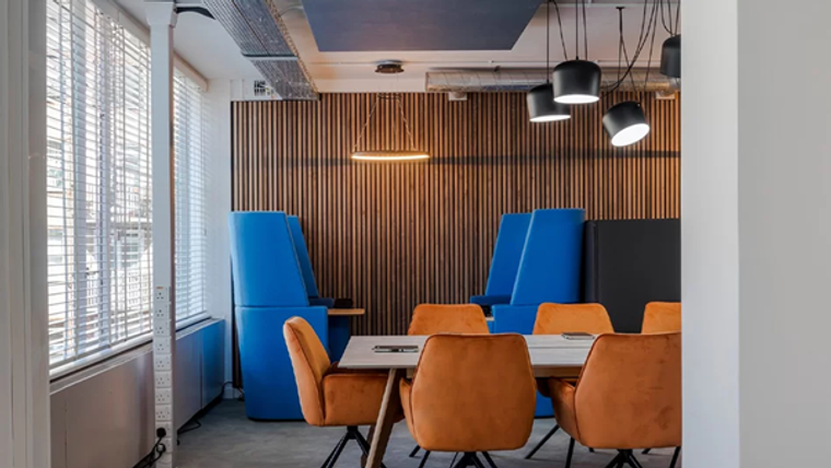 Mavi ve turuncu renklerde oturma alanları, ahşap duvar ve modern aydınlatmalarla döşenmiş bir ofis iç mekan.