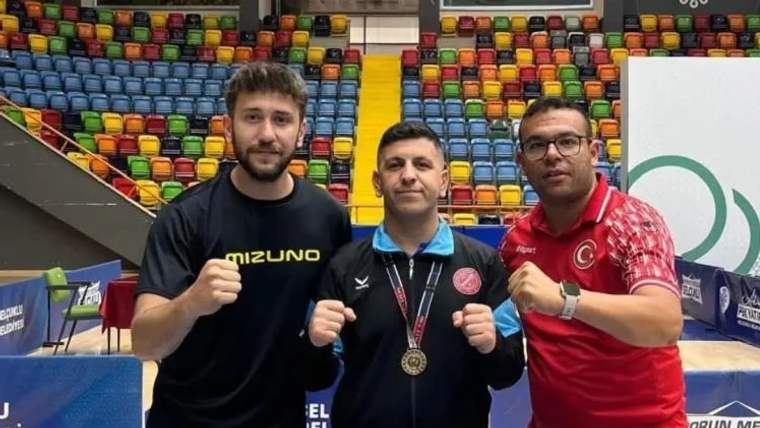 Üç kişi, bir spor salonunda madalya ile poz veriyor; arka planda renkli koltuklar var.