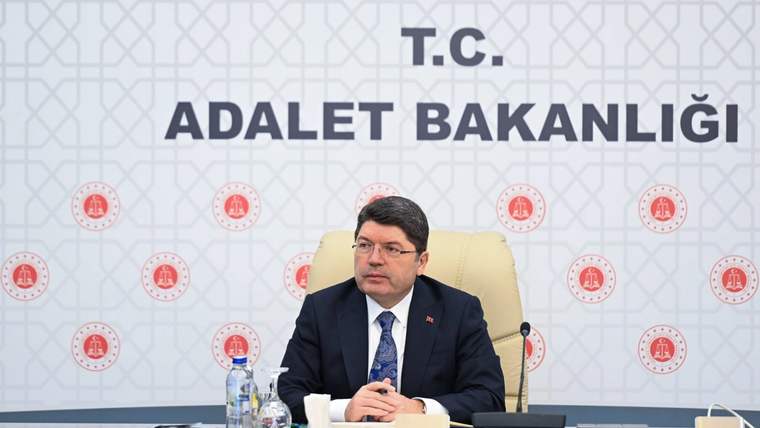 Adalet Bakanlığı yazılı panonun önünde takım elbiseli bir kişi, masa başında oturuyor.