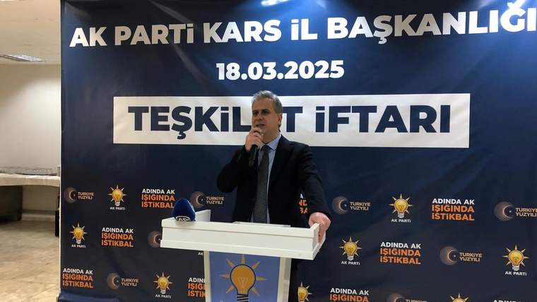 Kürsüde konuşan bir kişi, üzerinde “AK Parti Kars İl Başkanlığı” ve “Teşkilat İftarı” yazılı pankartın önünde duruyor.