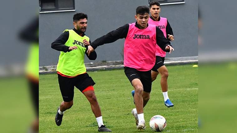 Antrenman yapan futbolcular, pembe yelek giymiş ve topa doğru koşuyorlar.
