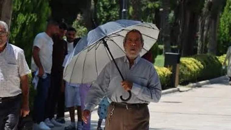 Beyaz bir şemsiye tutan yaşlı bir adam, parkta yürüyüş yapıyor.