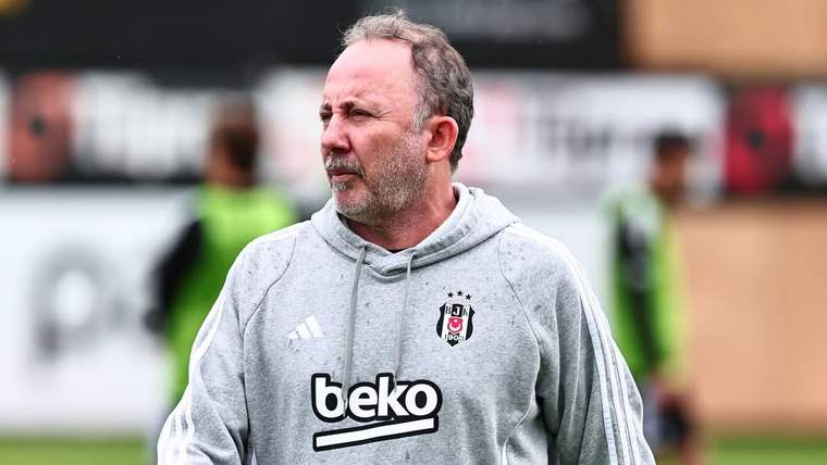 Beşiktaş armalı ve "beko" yazılı eşofman üstü giyen bir kişi, futbol sahasında yürüyor.