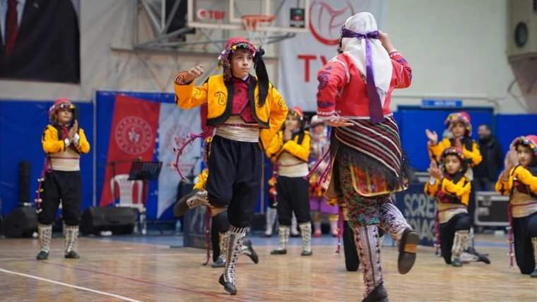Spor salonunda geleneksel kıyafetler giyen çocuklar, ellerindeki mendillerle halk oyunu oynuyor.